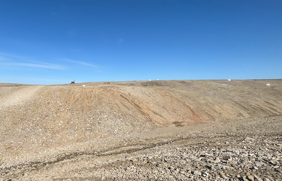 Figure 3: Photo of the Chinook copper deposit area looking north, across the gully from the Lightning Ridge Prospect. The extensive rust-coloured staining indicates an outcropping of copper sulfide. Also visible in the photo are a diamond drilling rig (left, middle) and several white bulk bags used for transporting drill samples.  